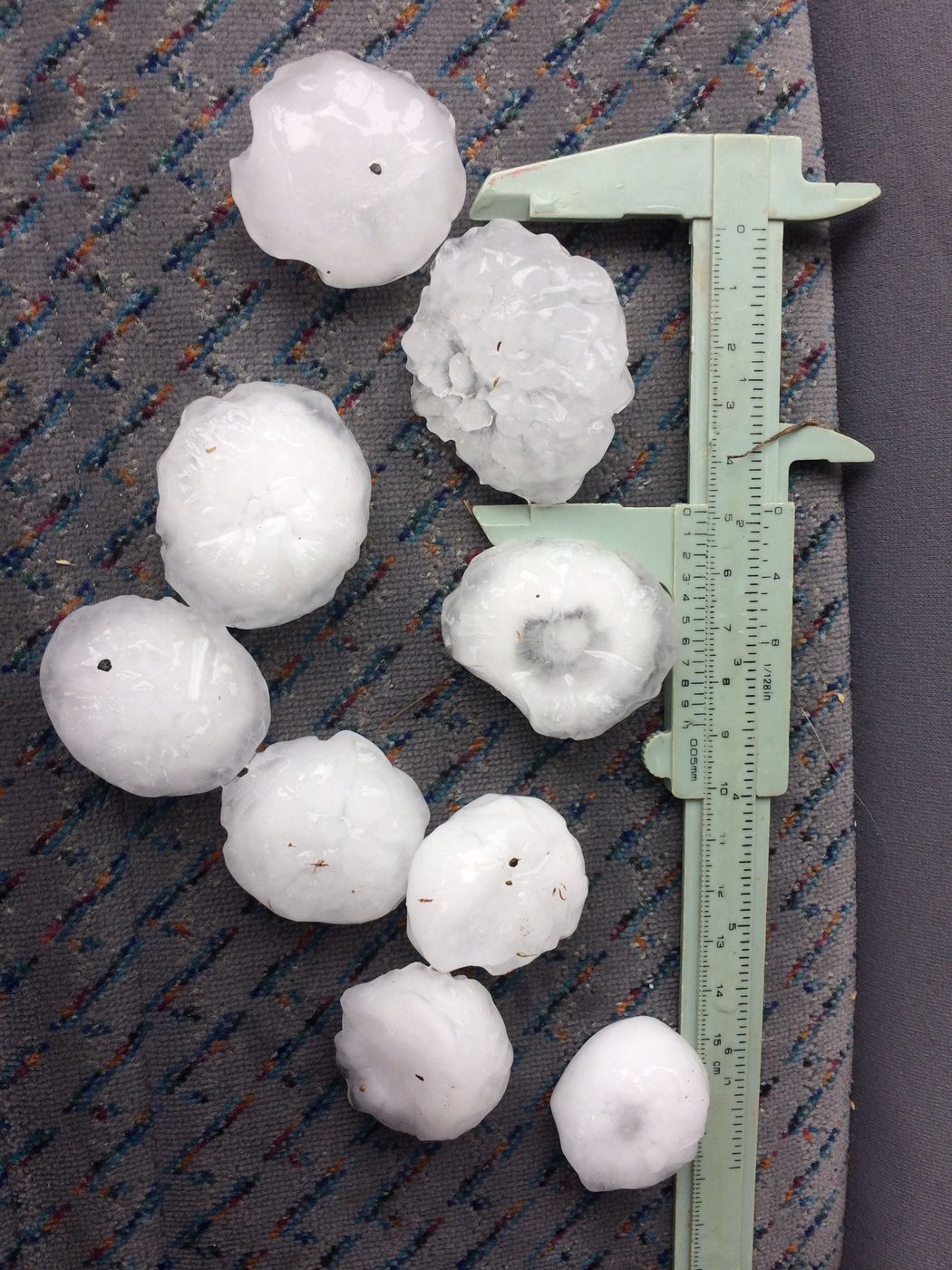Six large round hailstones lined up beside a steel ruler
