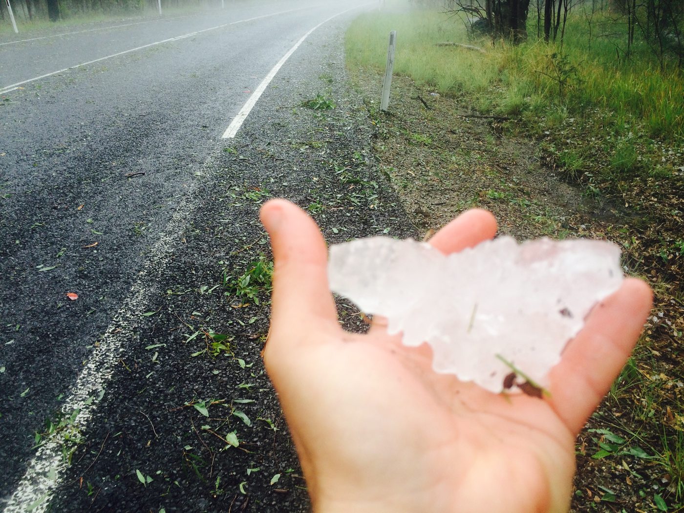 A large irregular hailstone held in a hand beside a wet road