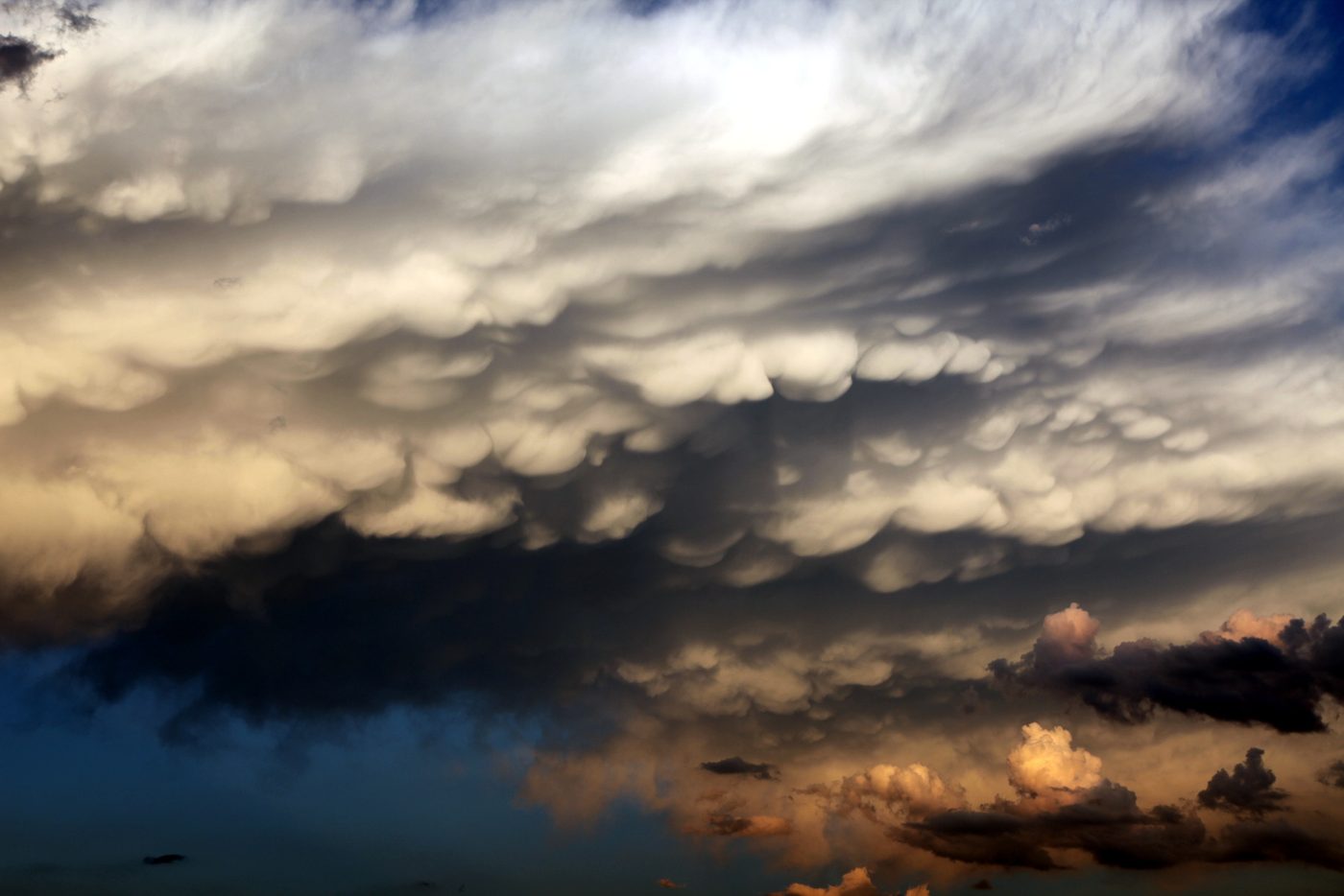 Mammatus clouds hanging beneath a storm lit by warm light