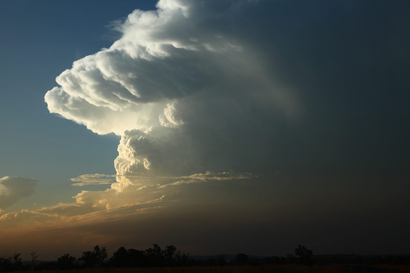A supercell tower with a flat anvil top in a teal and orange sunset sky